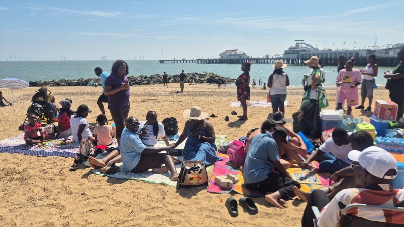 Church members relaxing together on the sand at the church beach trip, with a pier in the distance